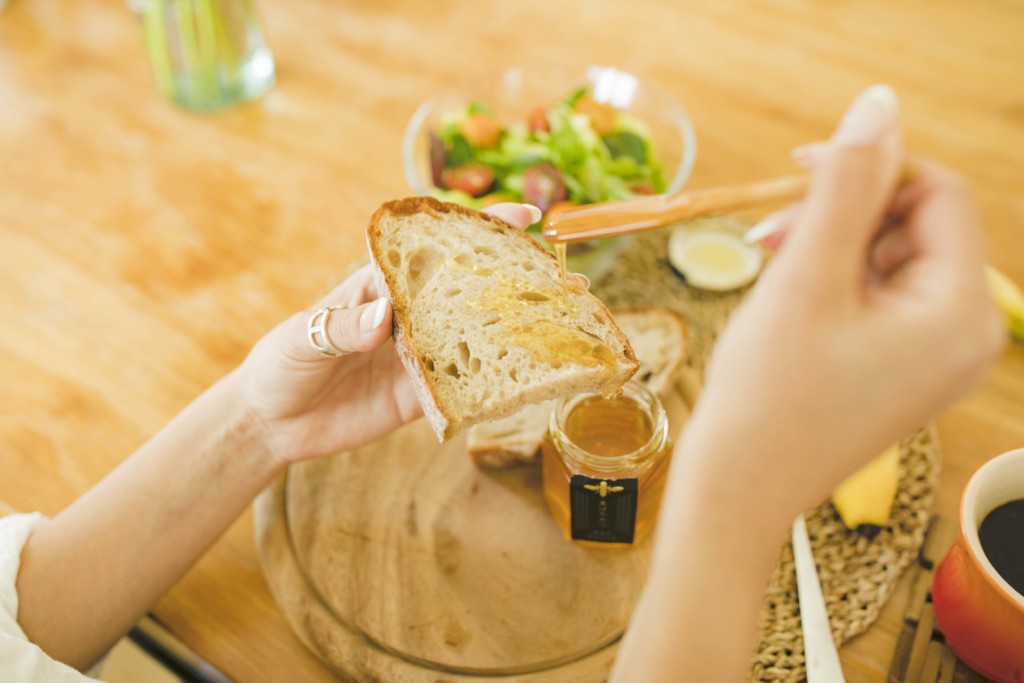 パンに蜂蜜をかけて朝食を食べる女性